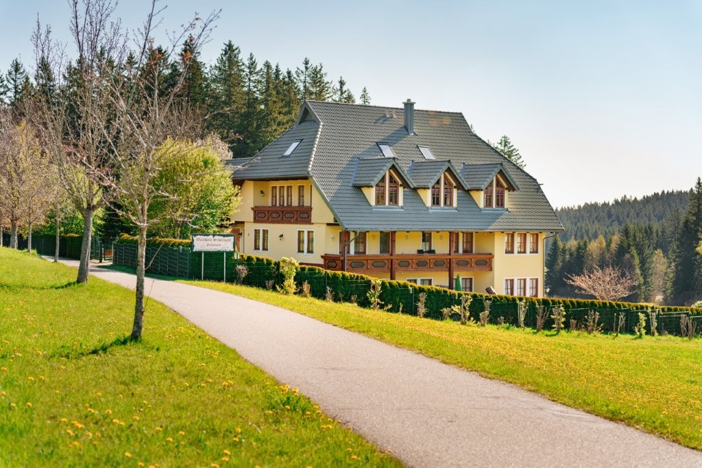 Haus mit Holzbalkonen in sonniger, grüner Schwarzwaldlandschaft